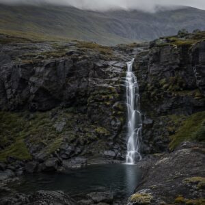 A narrow waterfall descends through mossy volcanic rock.